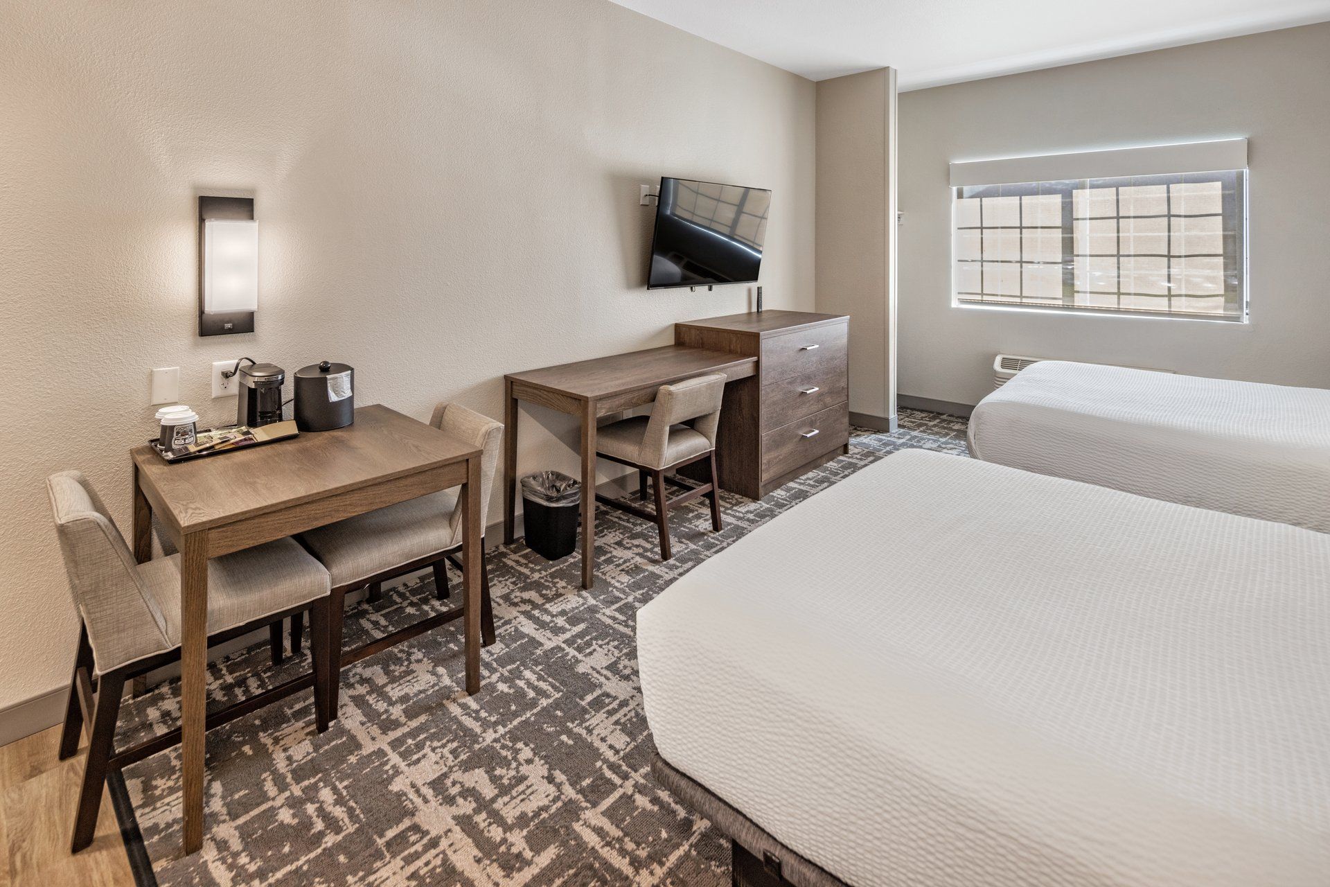 A hotel room with a desk, chair, two beds, a TV, and a window.