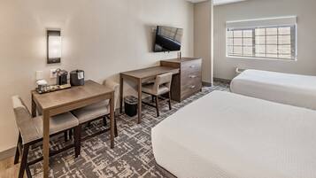 A hotel room with a desk, chair, two beds, a TV, and a window.