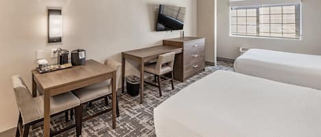 A hotel room with a desk, chair, two beds, a TV, and a window.
