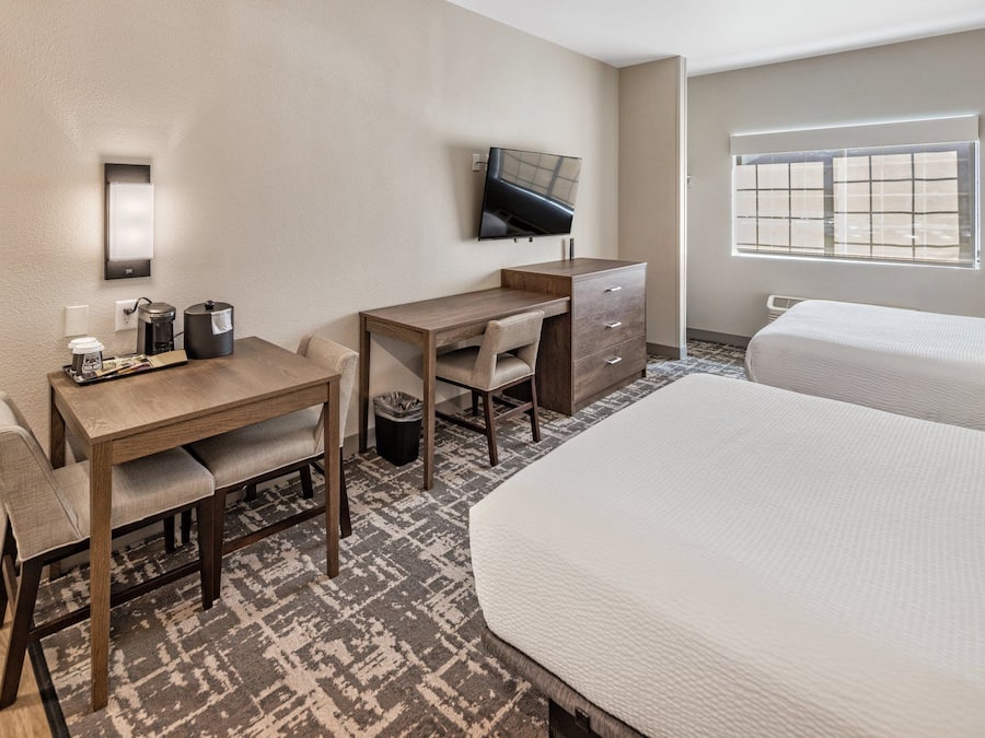 A hotel room with a desk, chair, two beds, a TV, and a window.