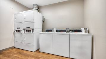 A laundry room with stacked washers and dryers, a vent on the ceiling, and wooden flooring.