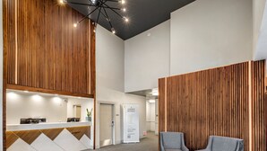 Un espace d’accueil avec un mur revêtu de panneaux en bois, un comptoir d’accueil, deux fauteuils et un luminaire moderne au plafond.
