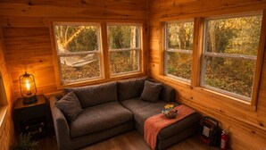 A cozy cabin interior with a sectional sofa, a small table, and a hammock by the windows.