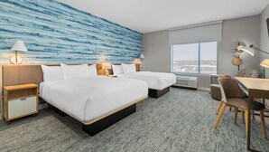 Habitación de hotel con dos camas, un escritorio y vistas a la ciudad.