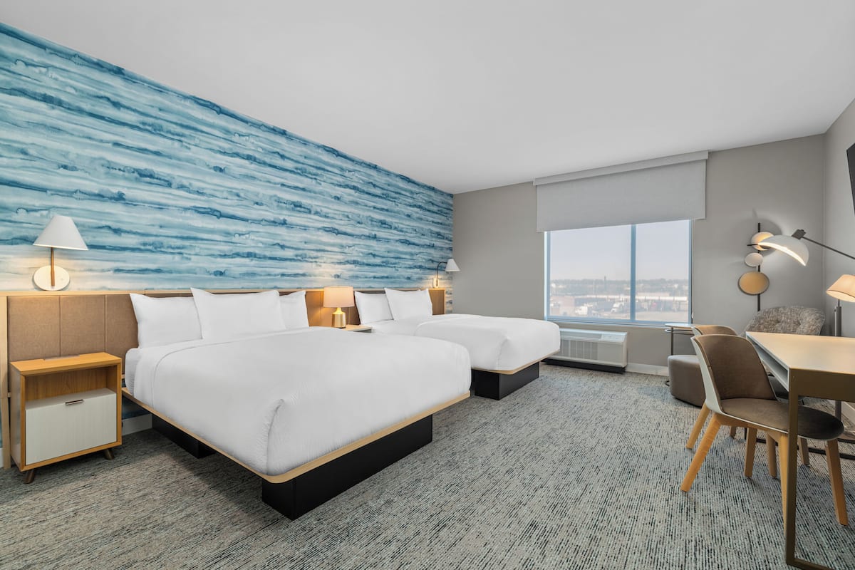 Habitación de hotel con dos camas, un escritorio y vistas a la ciudad.