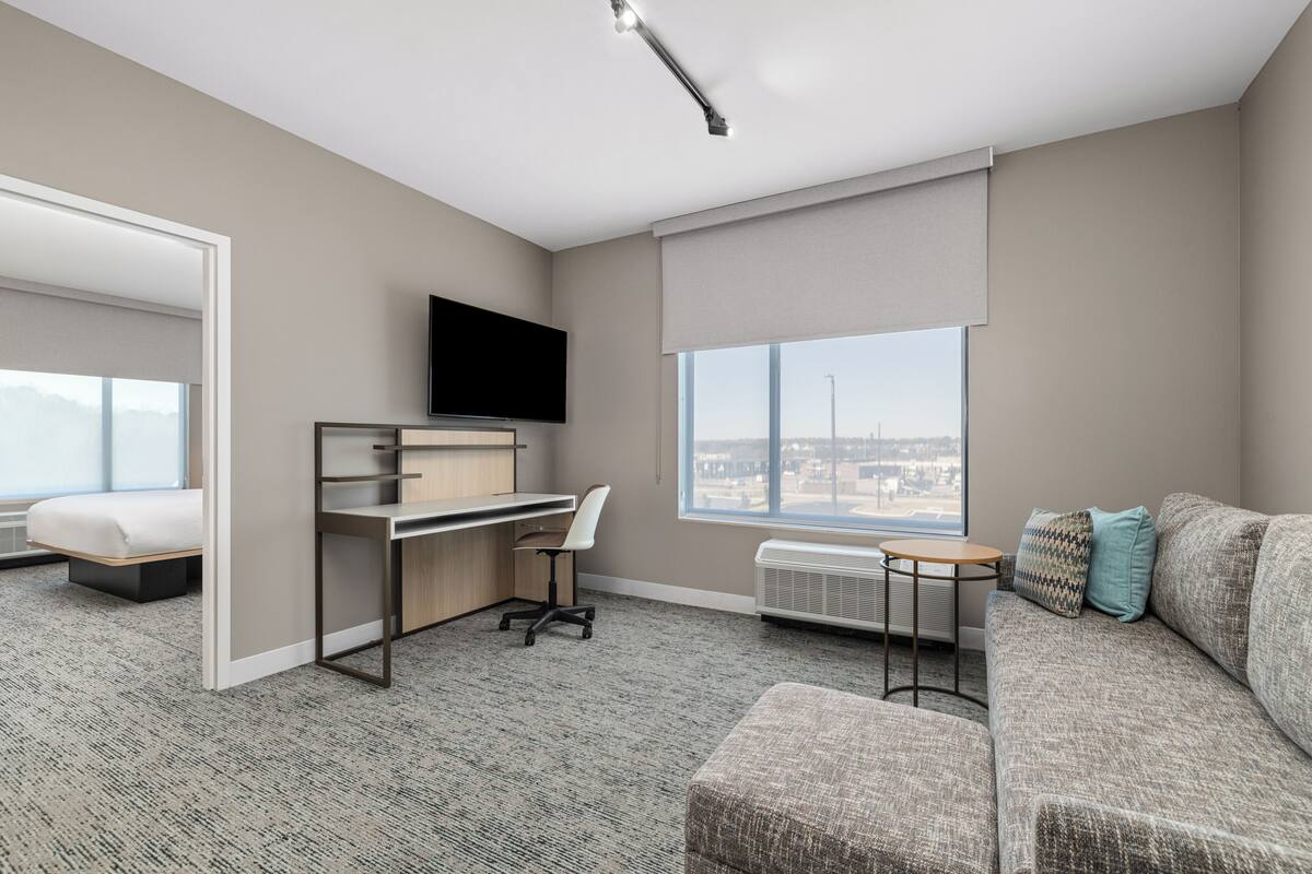 Una habitación de hotel moderna con escritorio, sofá, televisión y un ventanal con vistas a la ciudad.