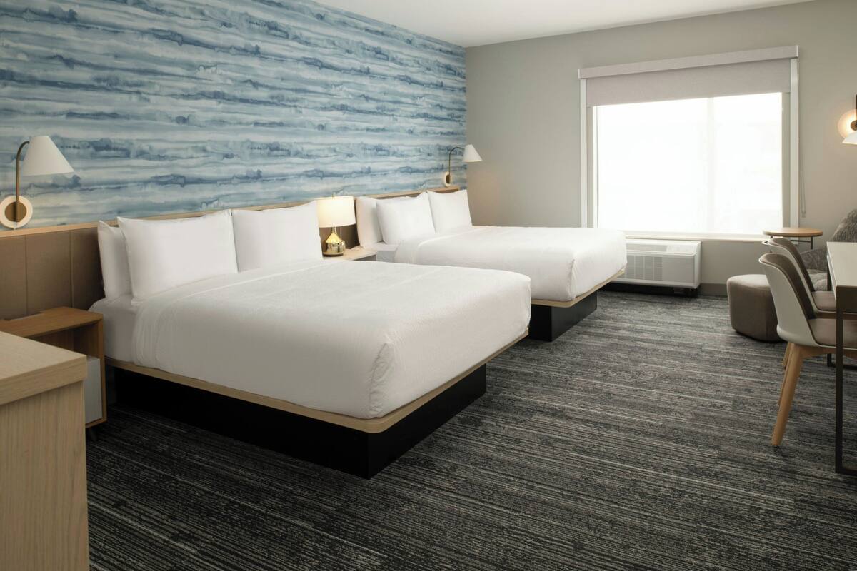 Habitación de hotel con dos camas, un escritorio, una silla y un ventanal grande.
