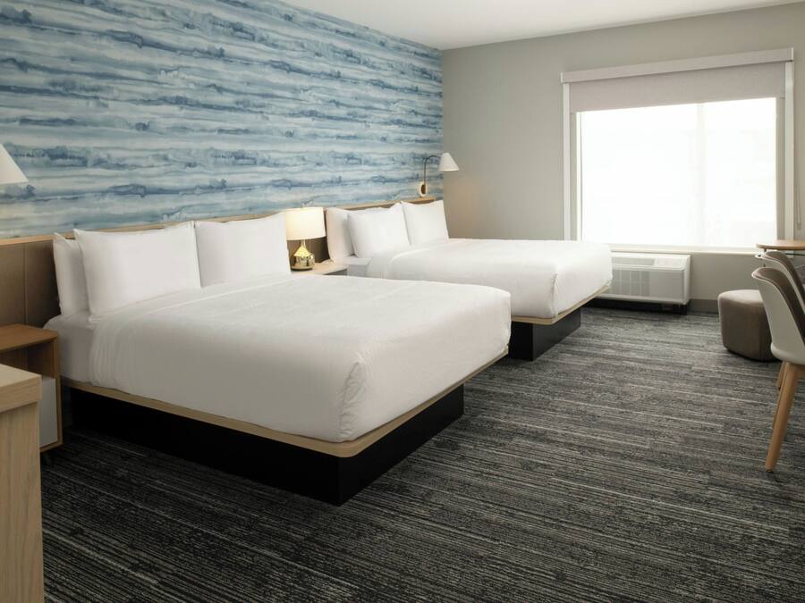 A hotel room with two beds, a desk, a chair, and a large window.