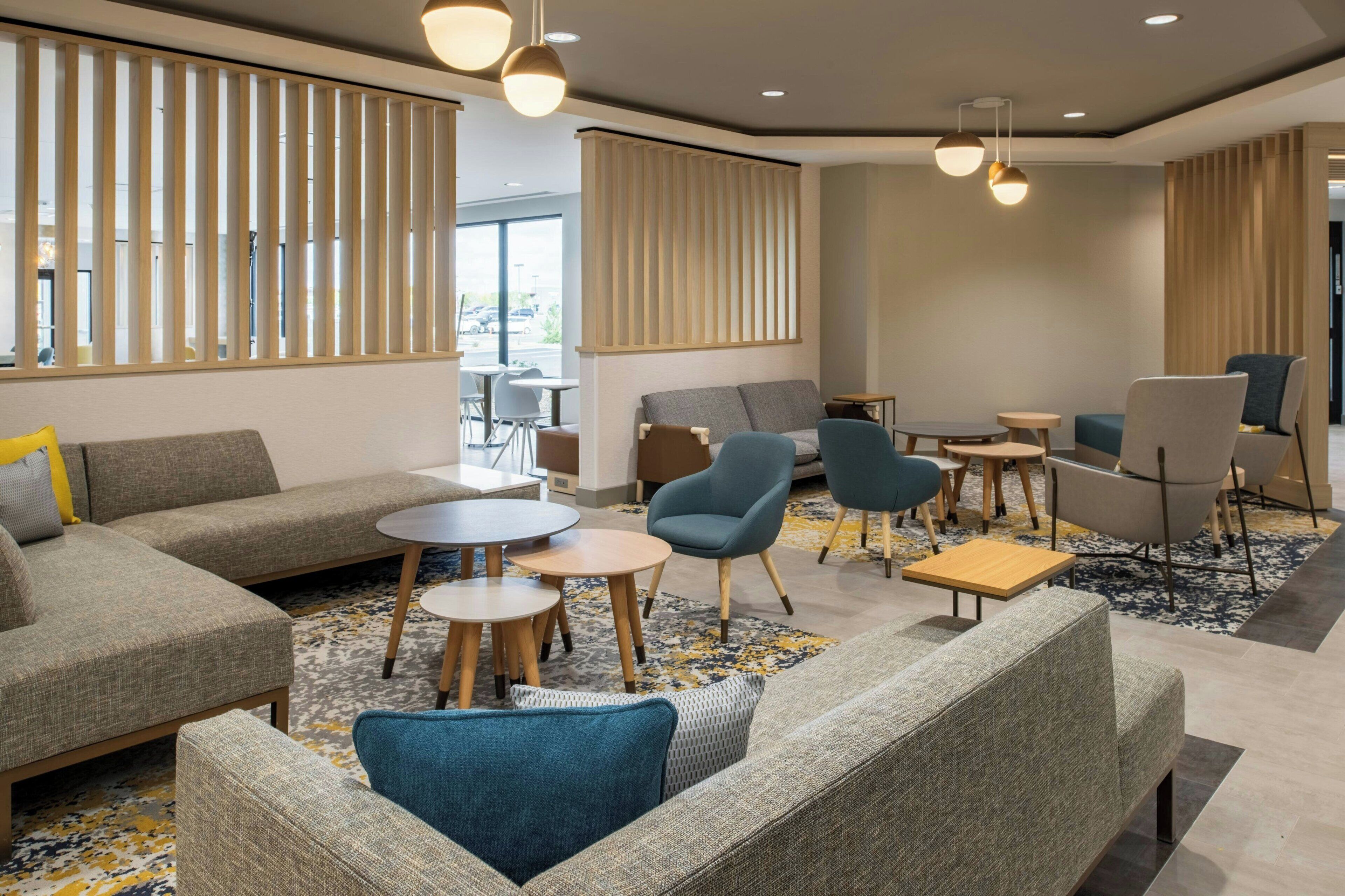 A modern lounge area with sofas, armchairs, and tables, featuring a neutral color palette and natural light.