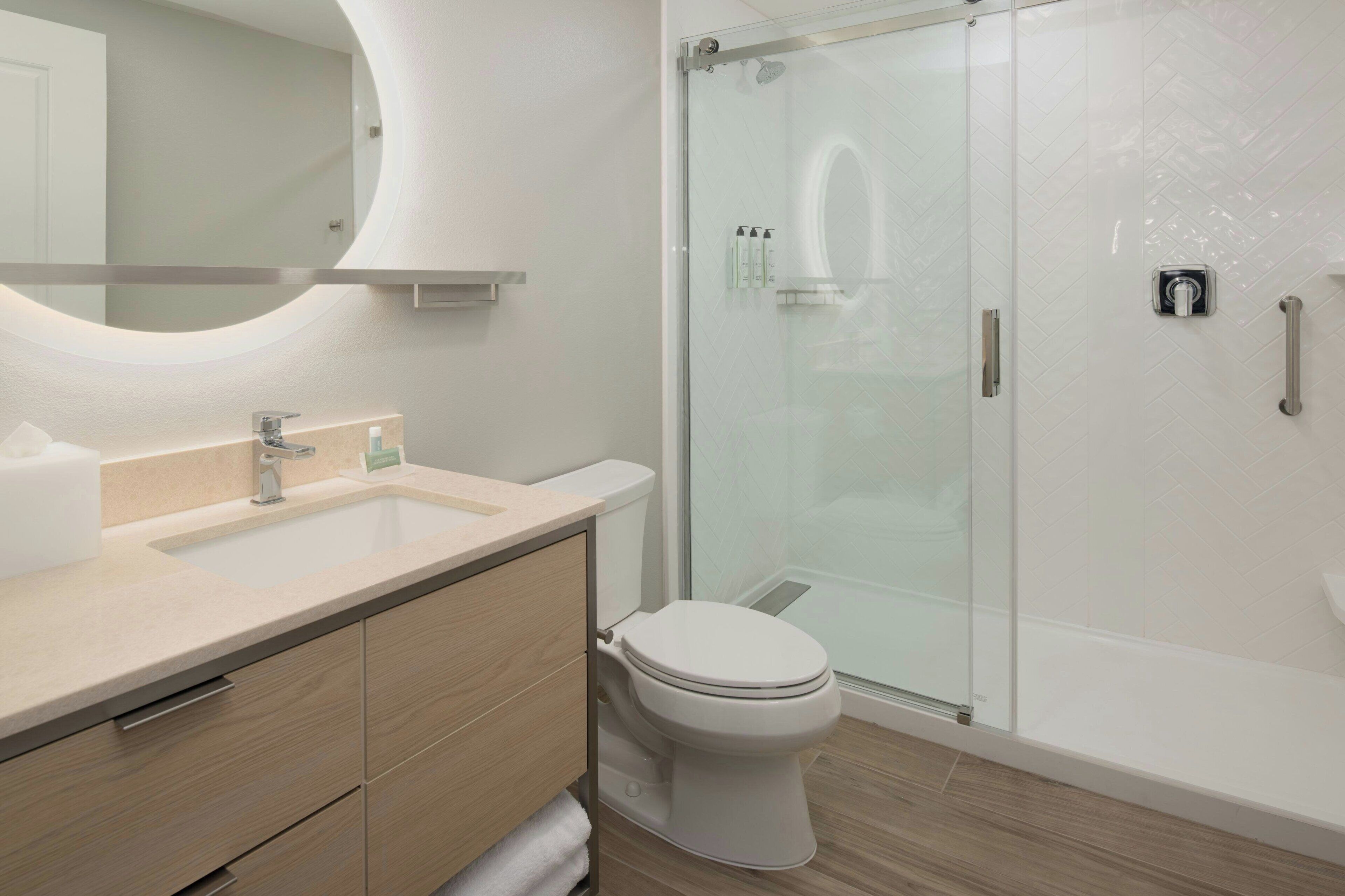 A modern bathroom with a glass-enclosed shower, a white toilet, and a beige vanity with a mirror.