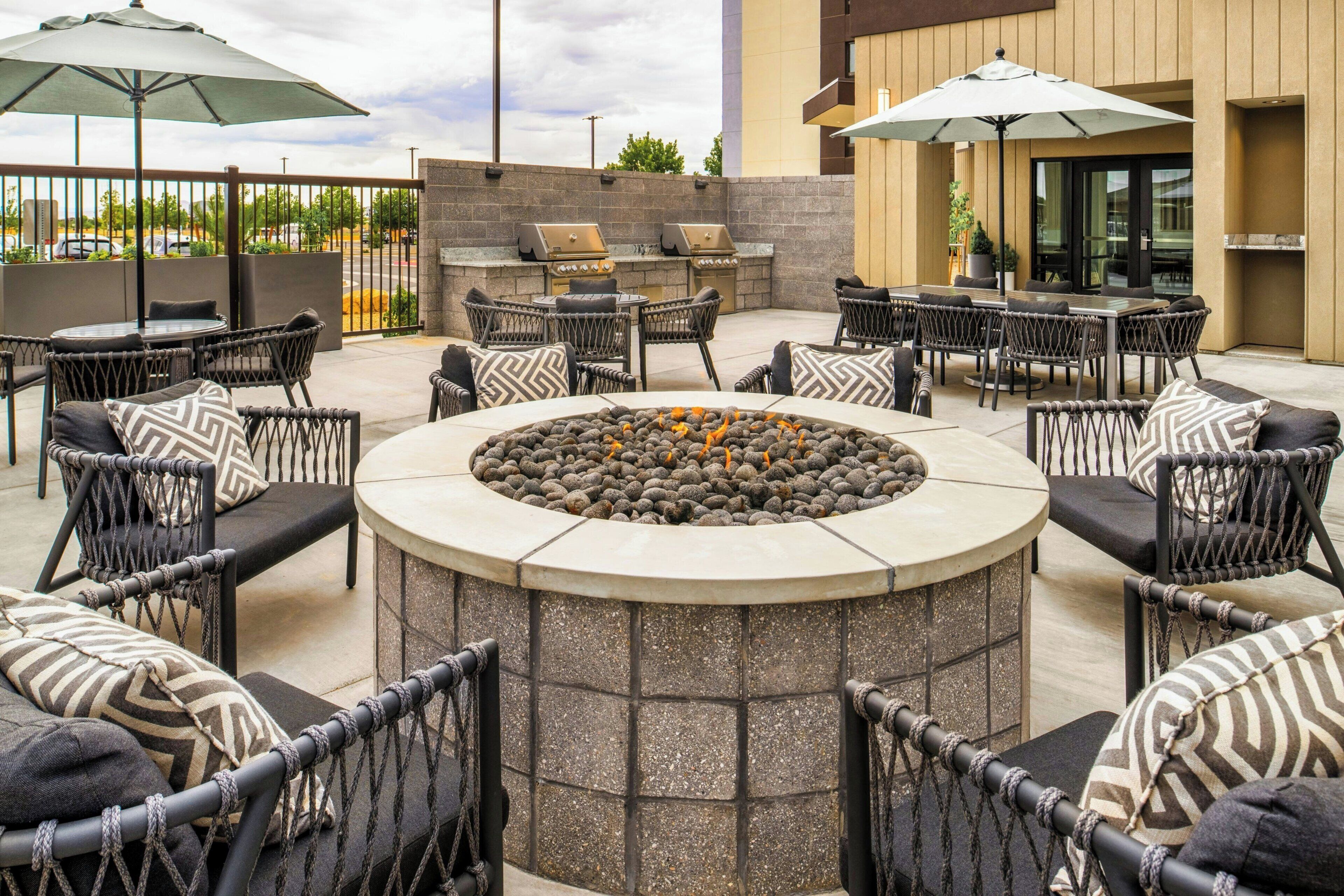 An outdoor patio with round tables, wicker chairs, and a central fire feature.