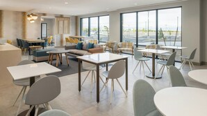 Un hall d’hôtel moderne offrant différents types de sièges, notamment des canapés, des fauteuils et des tables. De grandes fenêtres donnent sur le parking extérieur.
