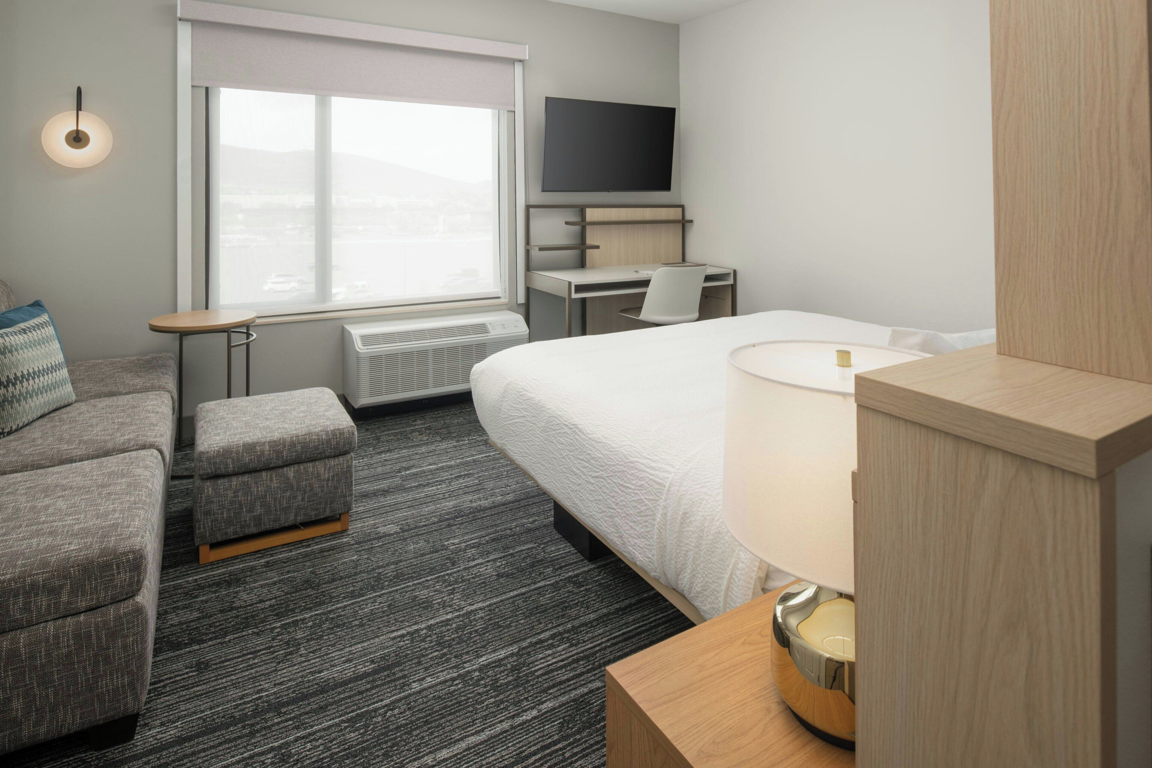 Ein Hotelzimmer mit Bett, Schreibtisch, Stuhl, kleinem Tisch, Fernseher und einem Fenster mit Aussicht.