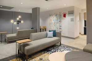 Un área de descanso moderna con un sofá gris, una mesita y un elemento decorativo en la pared.
