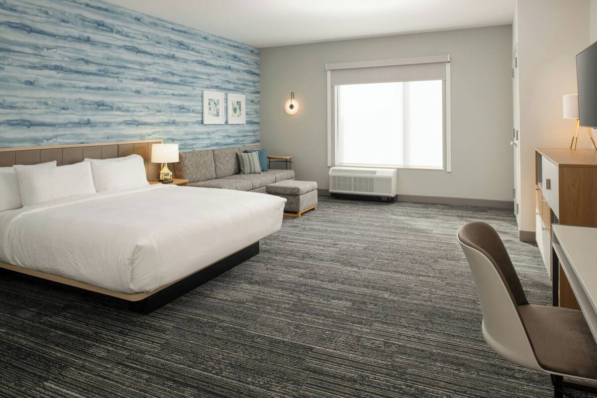 Una habitación de hotel con una cama grande, un sofá, un escritorio y una televisión.