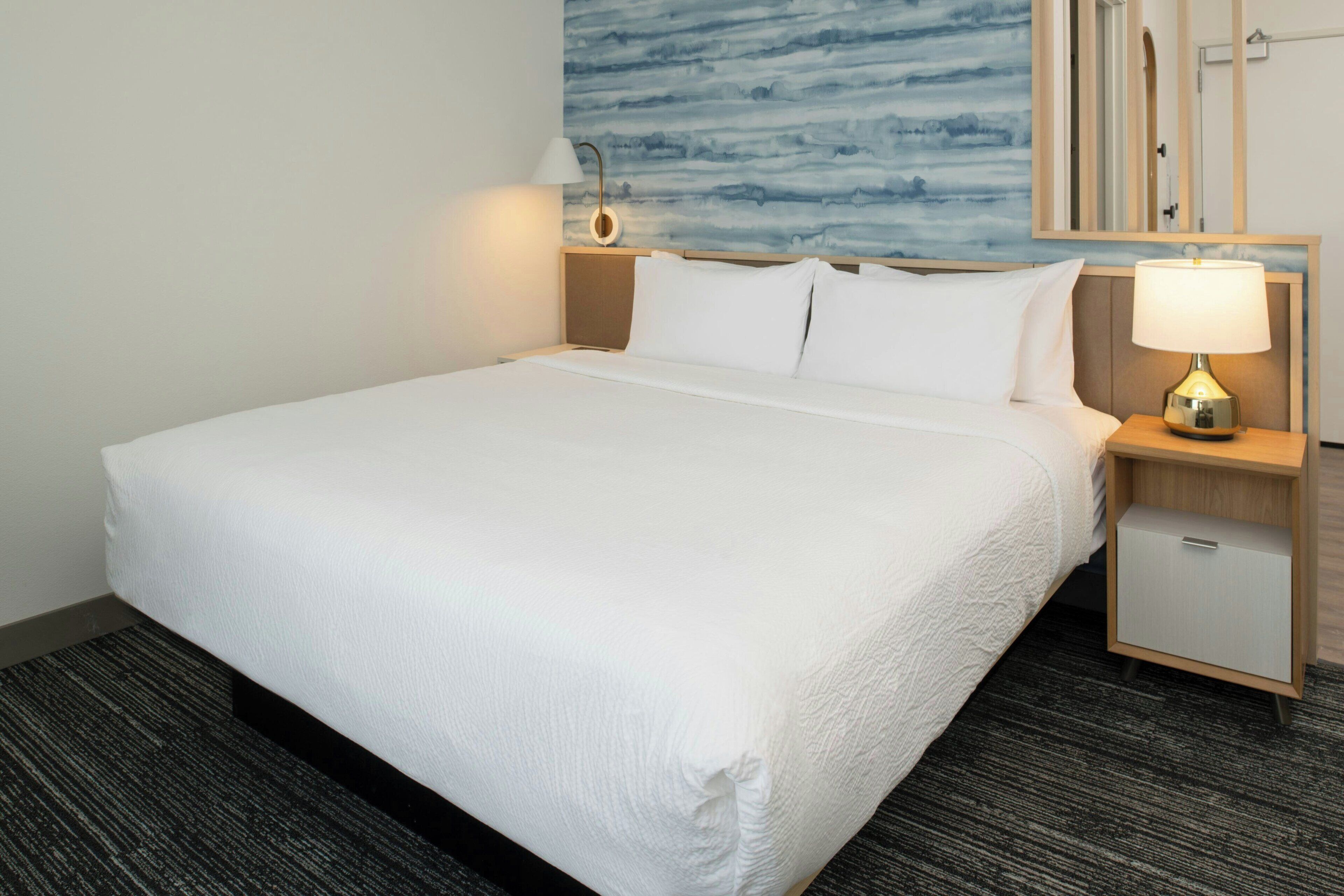 A neatly made bed with white linens, a bedside table with a lamp, and a small cabinet.