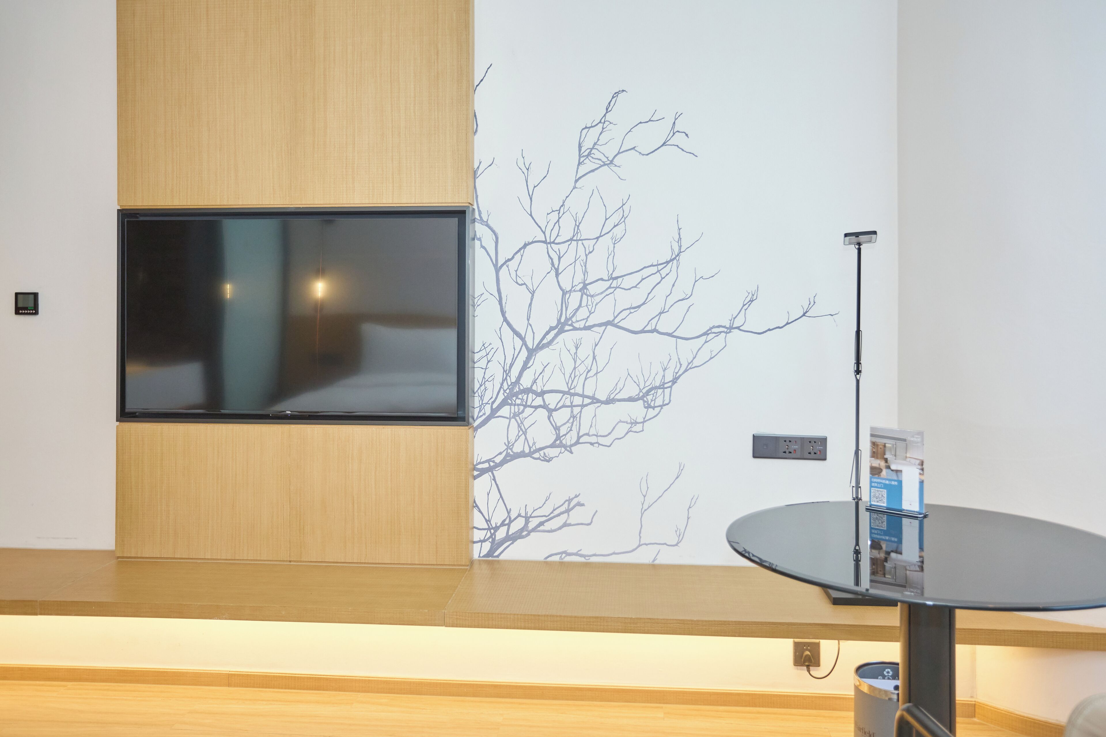 A modern room with a large flat-screen TV mounted on a wooden panel, a wall-mounted projector, and a round table with a small box on it.