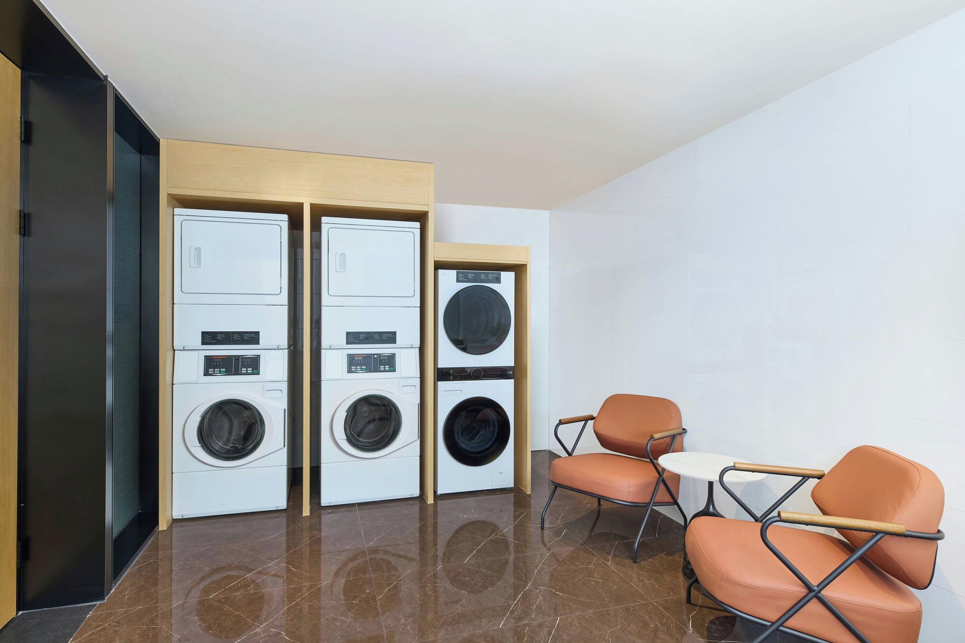 A laundry room with stacked washers and dryers, a small table, and two chairs.