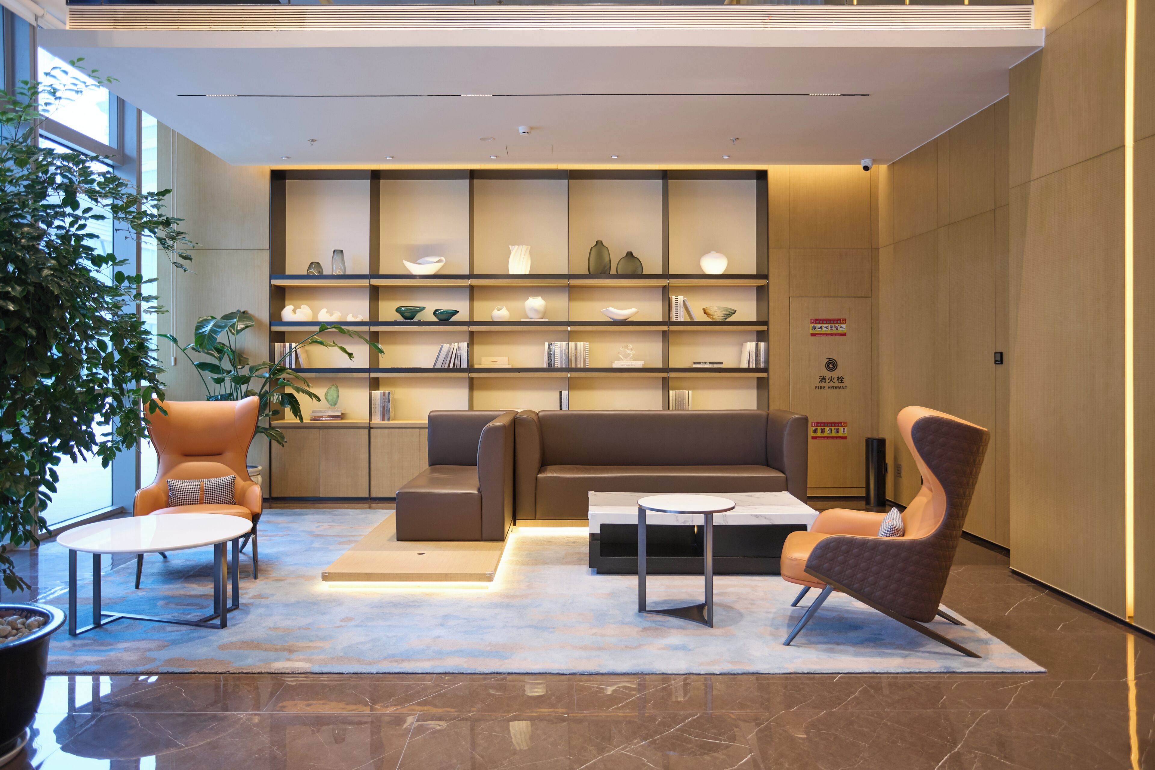 A modern lobby with a sofa, chairs, a coffee table, a bookshelf, and a potted plant.