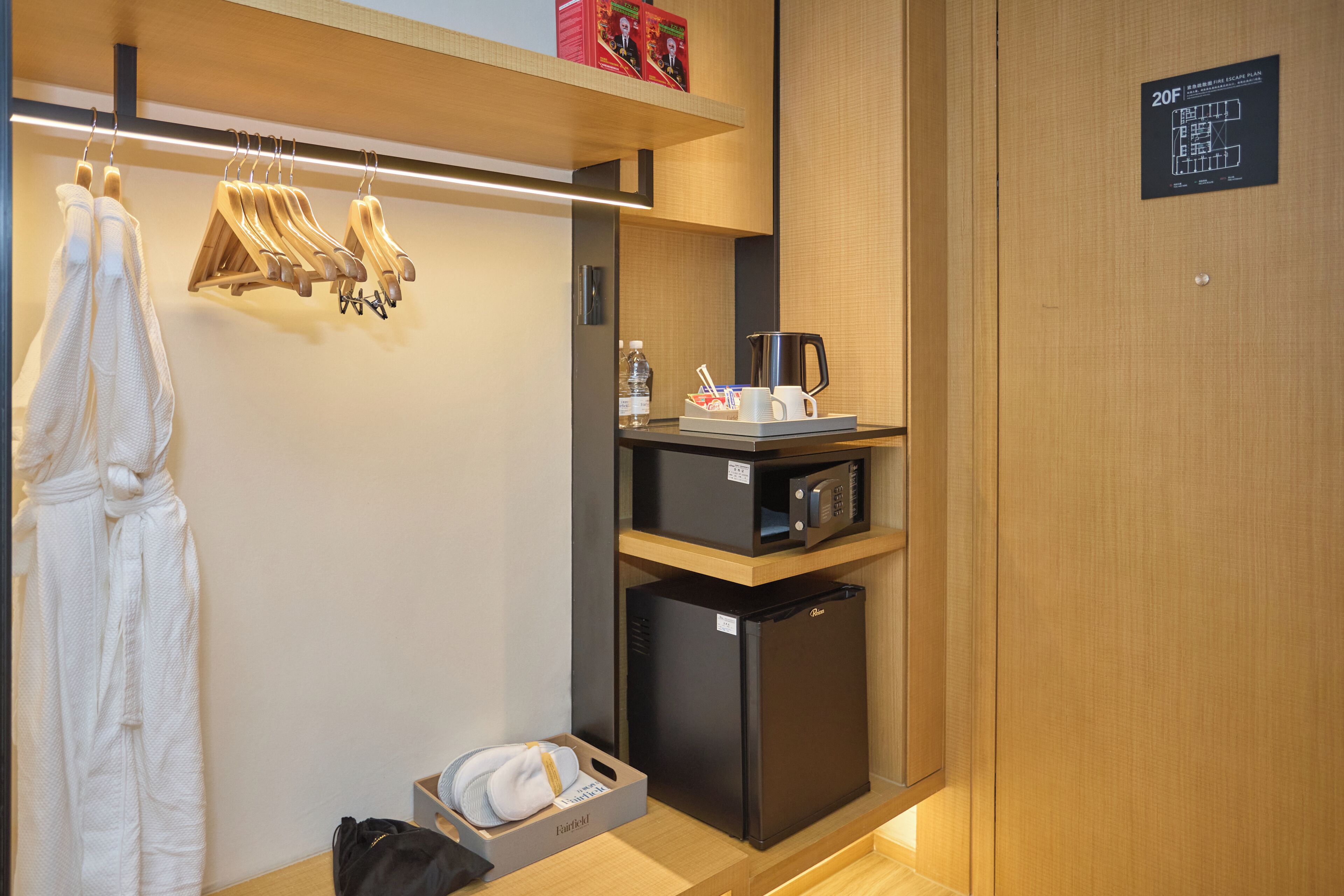 Ein Hotelzimmer mit Holzschrank, Mikrowelle, Minikühlschrank, Tablett mit Kaffeemaschine und aufgehängtem Bademantel.
