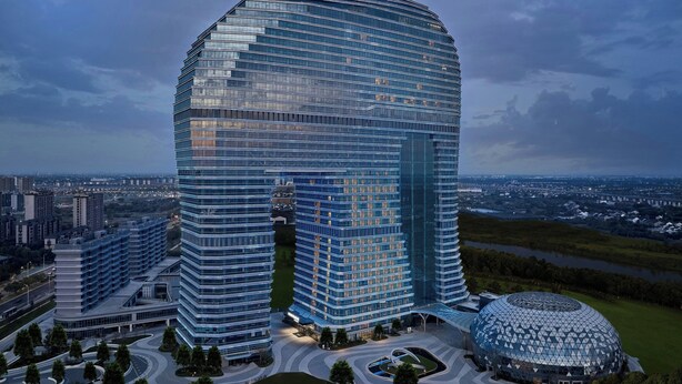 A modern, curved skyscraper with a glass facade, surrounded by a landscaped area with a circular building nearby. - Fairfield By Marriott Huzhou Nanxun (Huzhou)