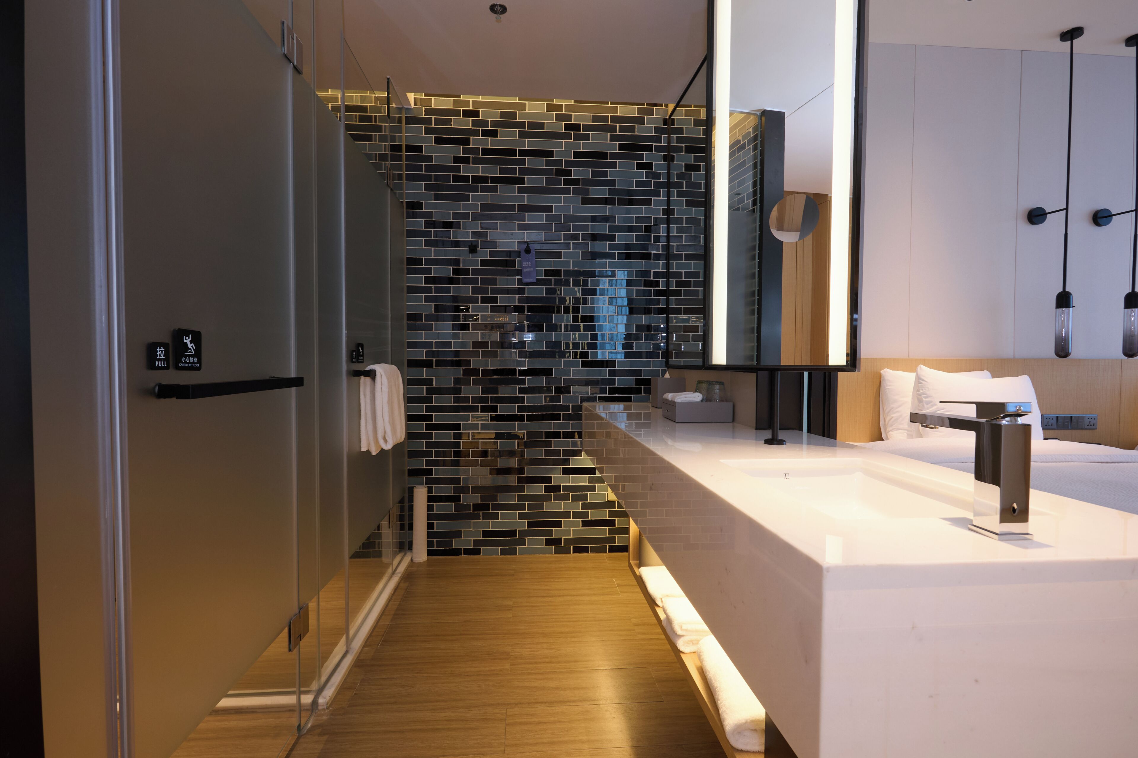 A modern bathroom with a glass shower enclosure, a wooden floor, a white sink, and a large mirror.