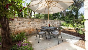 Un patio al aire libre con un muro de piedra, una mesa redonda con sillas y una sombrilla.