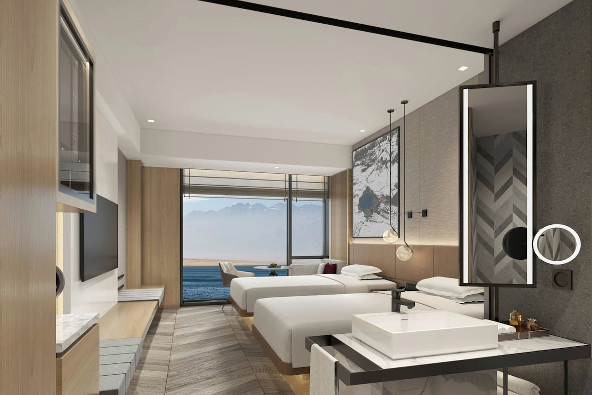 Una habitación de hotel moderna con una cama grande, una zona de estar independiente, un baño con un espejo amplio y vistas al mar.
