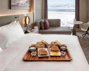 A hotel room with a bed, a bedside table with a lamp, a small round table, and a sofa.