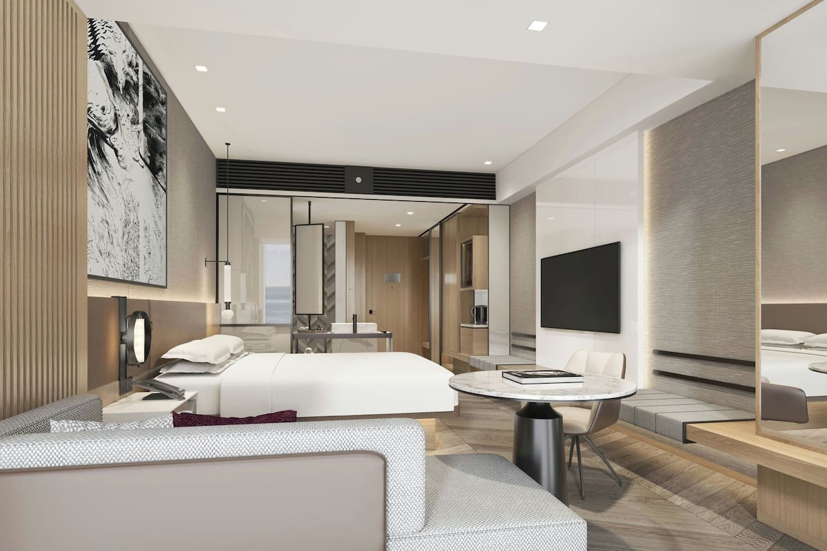 Una habitación de hotel moderna con una cama grande, una zona de estar con sofá y sillón, una pequeña mesa de comedor y un espejo amplio.