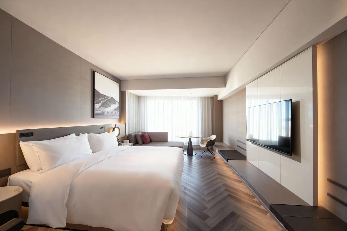 Una habitación de hotel moderna con una cama grande, televisión, sofá y mesa de comedor.