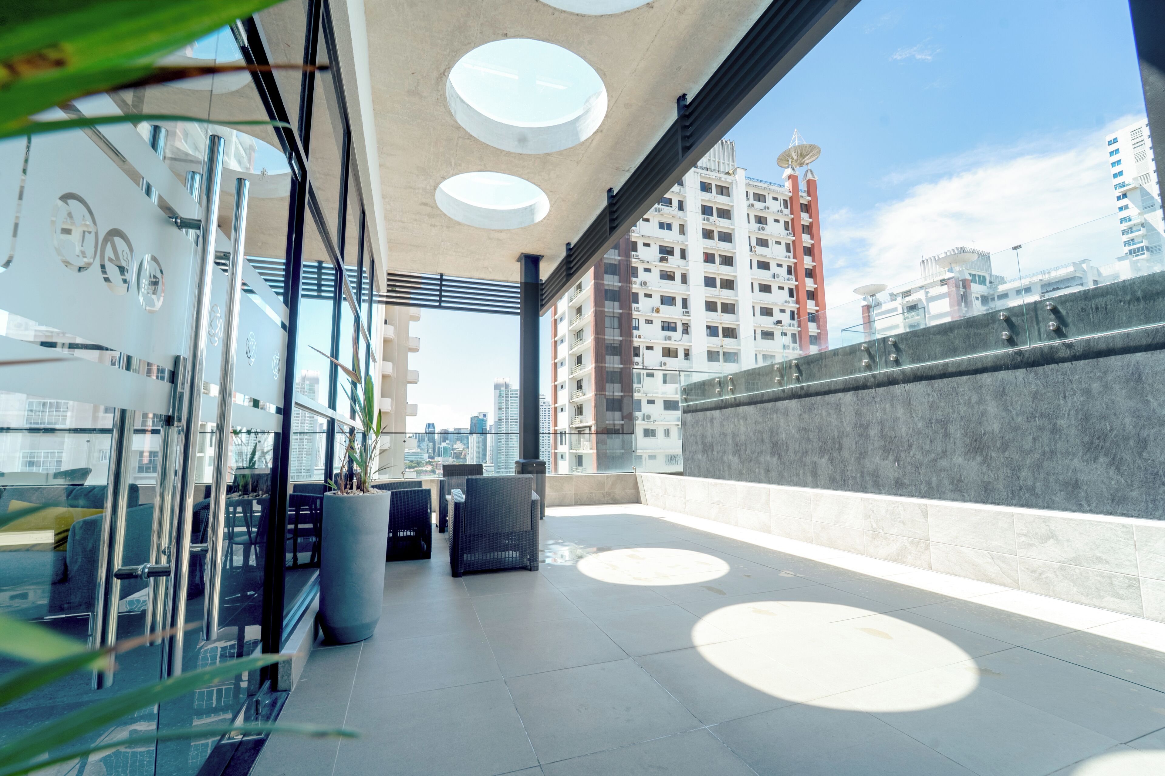 A modern rooftop terrace with glass walls, circular skylights, and a city view.