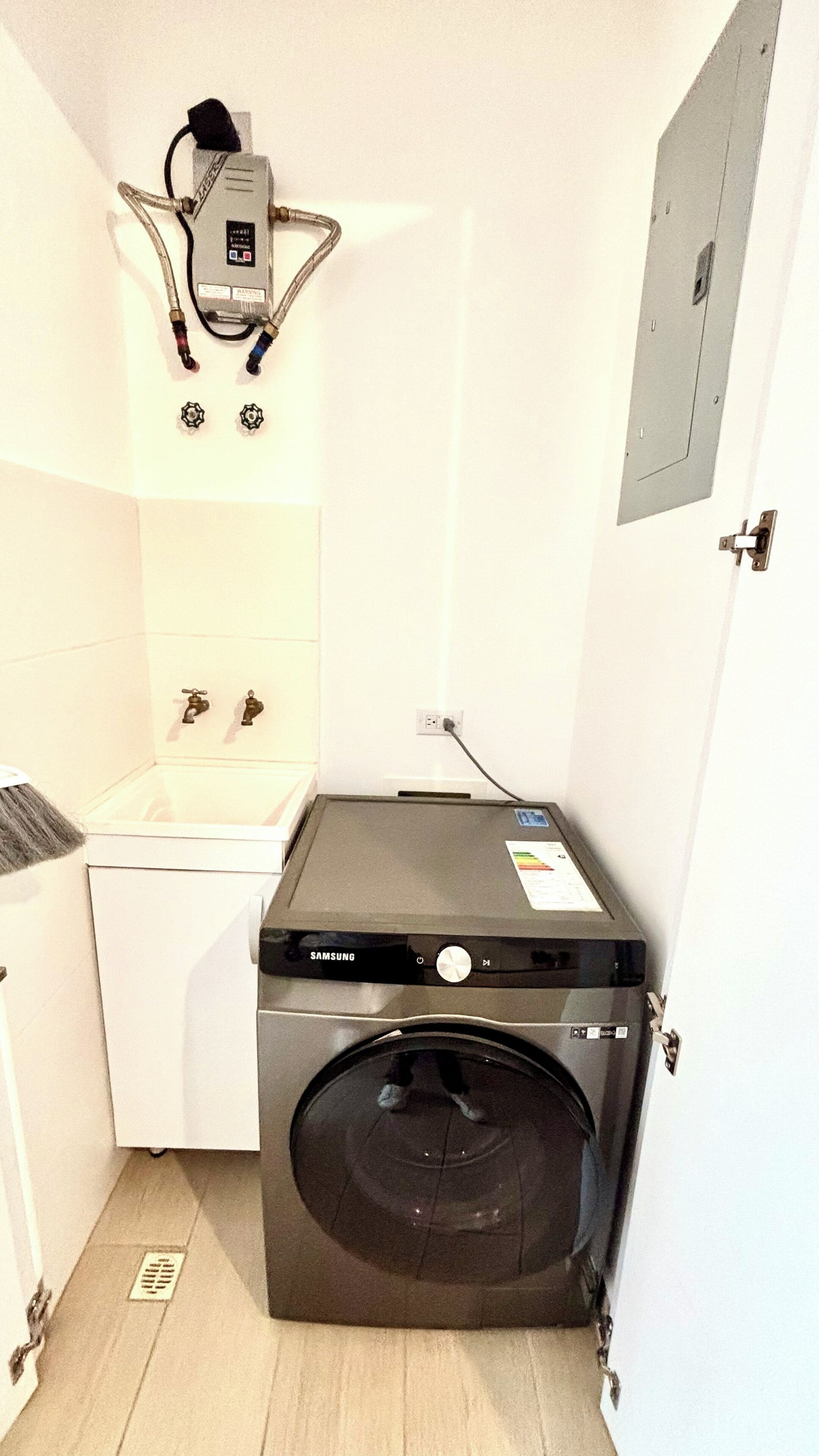 A compact laundry room with a front-loading washing machine, a small sink, and a heater mounted on the wall.