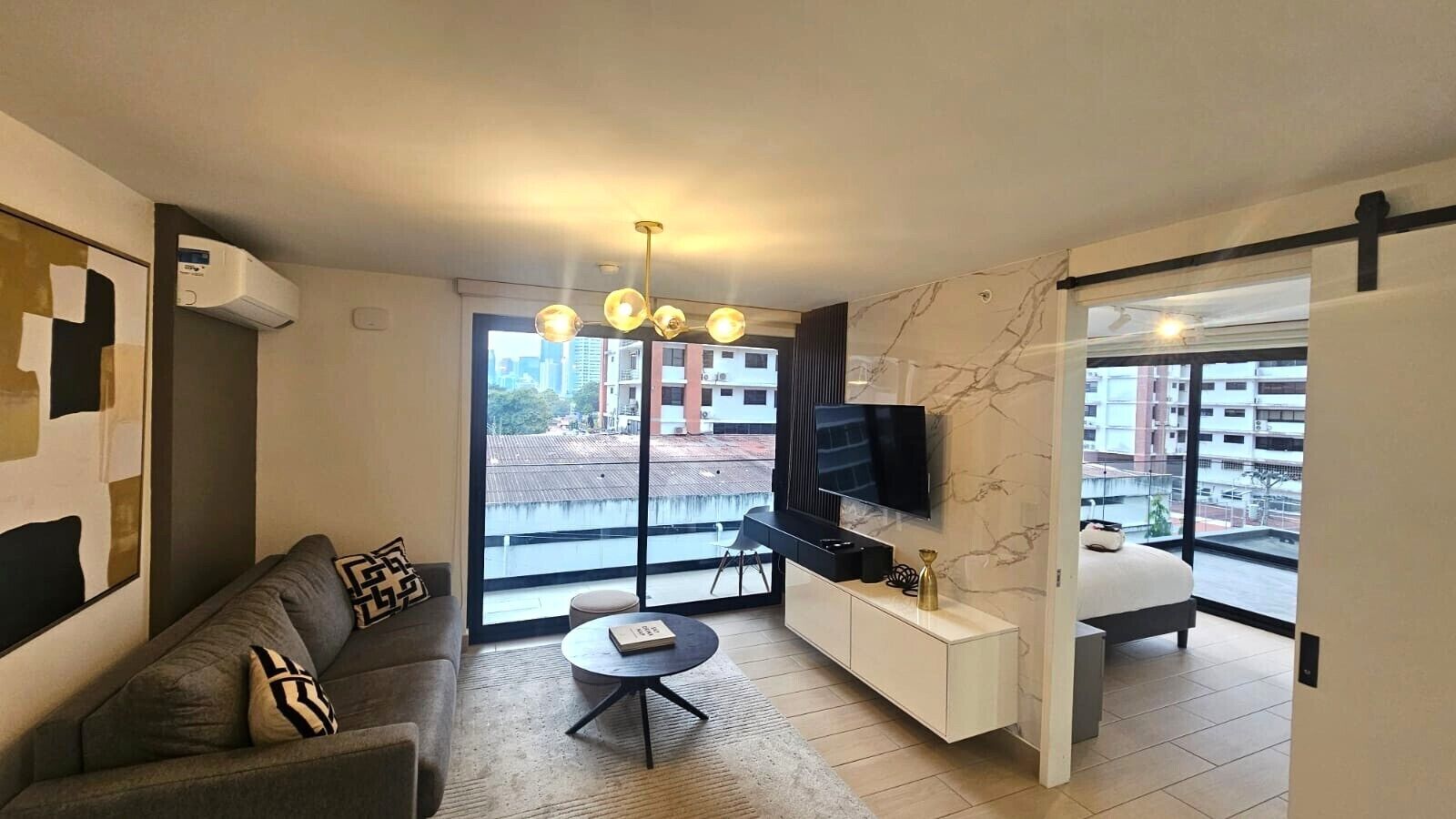 Una sala de estar moderna con sofá, mesa de centro, televisión y un balcón con vistas a la ciudad.