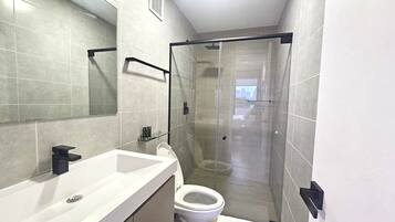 A modern bathroom with a glass shower enclosure, a white sink, and a toilet.