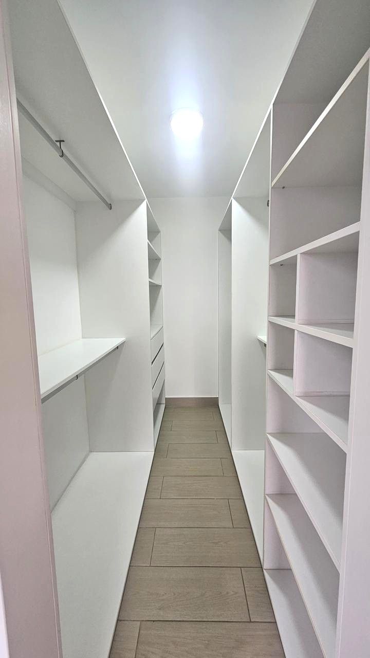 A narrow walk-through closet with white shelving units and a wooden floor.