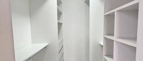 A narrow walk-through closet with white shelving units and a wooden floor.