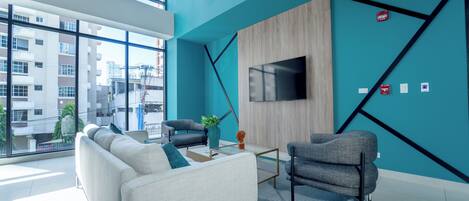 Un salon moderne avec un canapé, des fauteuils, une table basse et un téléviseur fixé au mur.
