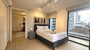 Ein modernes Schlafzimmer mit einem großen Bett, einem Nachttisch, einem an der Wand montierten Fernseher und einem Fenster mit Blick auf die Stadt.