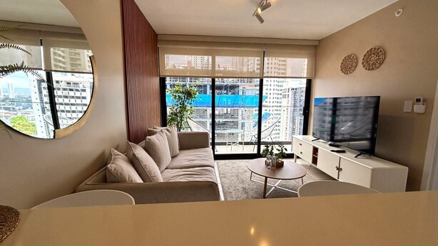 A modern living room with a sofa, a TV, a small table, and a balcony with a view of the city. - Living 73 Panamá by Boutique Apartments (Panama City)