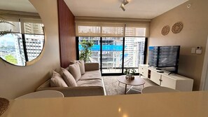 A modern living room with a sofa, a TV, a small table, and a balcony with a view of the city. - Living 73 Panamá by Boutique Apartments (Panama City)
