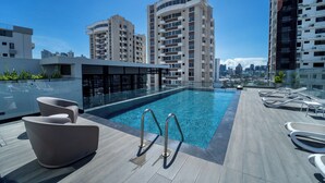 A rooftop swimming pool with modern lounge chairs and a city skyline in the background. - Living 73 Panamá by Boutique Apartments (Panama City)