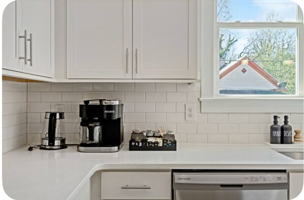 A kitchen with white cabinets, a coffee maker, a dishwasher, and a window with a view of a house. - Brand New 3Bed3Bath•Downtown•Spacious•Patio•Modern (Raleigh)