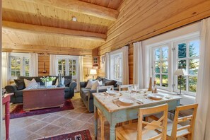 Hyggelig interiør i en hytte med træloft, et spiseområde med et bord til fire og en opholdsstue med to sofaer og et sofabord.