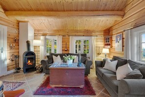 Et hyggeligt interiør i en træhytte med pejs, to sofaer, et sofabord og store vinduer.