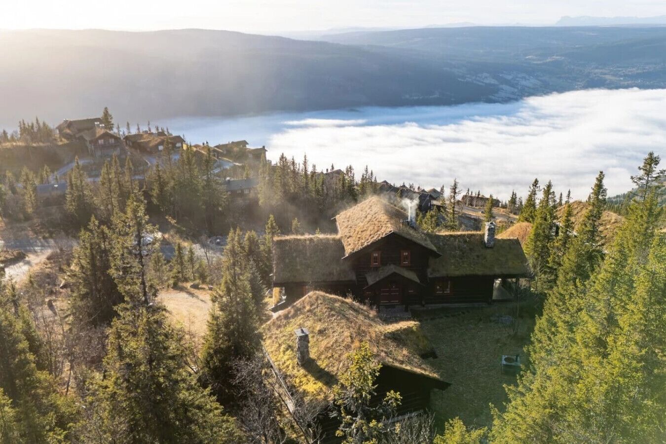 Eine Berglodge mit Strohgedeckten Dächern, umgeben von dichtem Wald und Blick ins Tal.