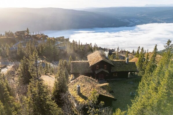 A mountain lodge with thatched roofs surrounded by dense forest and a view of a valley below.