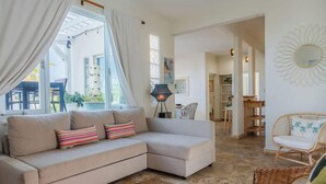 Un salon avec un canapé d’angle beige, un fauteuil en osier et une lampe sur pied.
