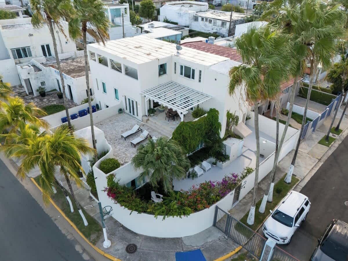 A modern building with a flat roof, a covered outdoor seating area, and a landscaped garden with palm trees and shrubs.