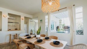Un espace repas avec une longue table, des chaises en osier et un luminaire suspendu.